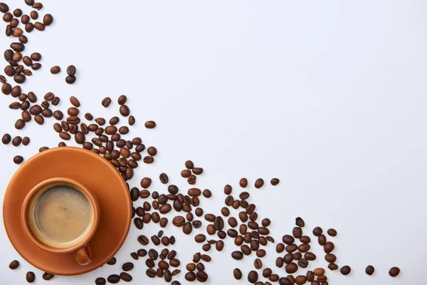 Vista superior de delicioso café na xícara perto de grãos espalhados no fundo branco com espaço de cópia — Fotografia de Stock