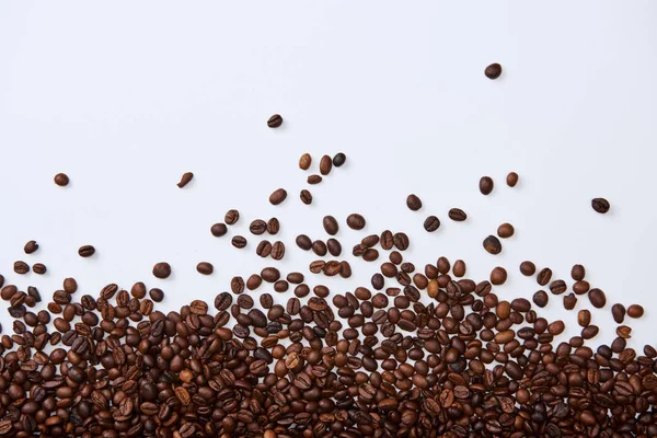 Top view of scattered brown roasted beans on white background — Stock Photo