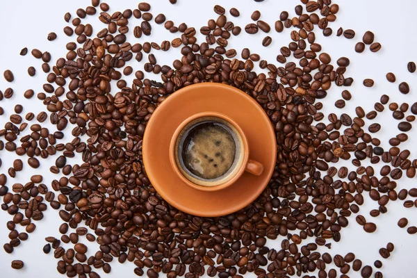 Vista dall'alto del caffè in tazza marrone sul piattino vicino ai fagioli tostati sparsi — Foto stock