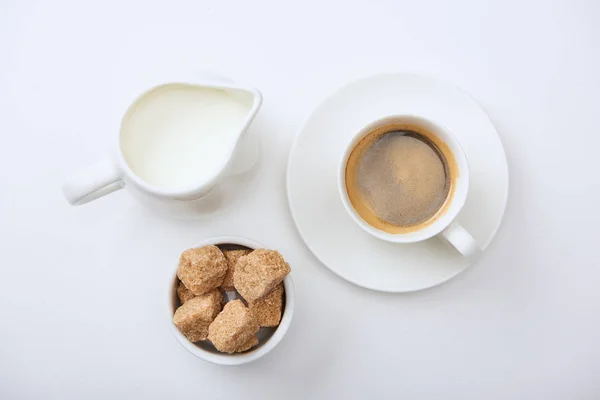 Vista superior de café saboroso na xícara perto de leite e açúcar mascavo no fundo branco — Fotografia de Stock