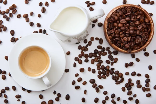 Top view of coffee near scattered roasted beans, wooden bowl and milk jug — Stock Photo