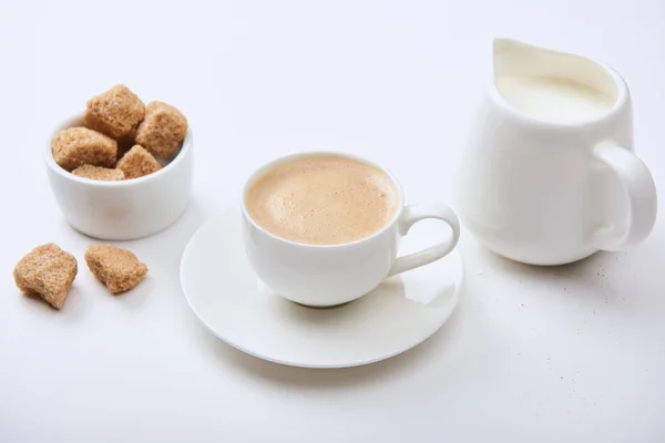 Tasty coffee in cup near milk and brown sugar on white background — Stock Photo