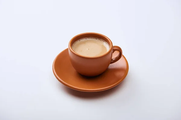 Delicioso café con espuma en taza marrón en platillo sobre fondo blanco - foto de stock
