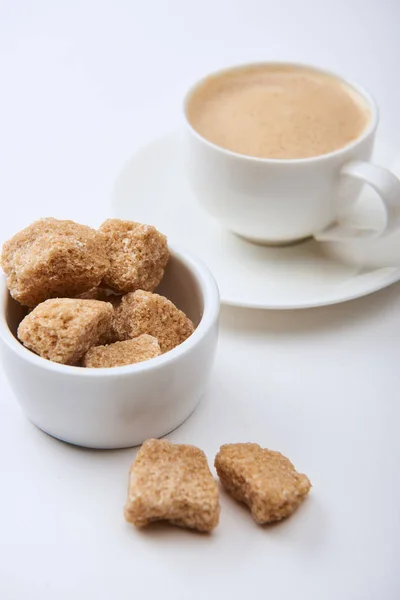 Leckeren Kaffee mit Schaum in Tasse auf Untertasse in der Nähe von braunem Zucker auf weißem Hintergrund — Stockfoto