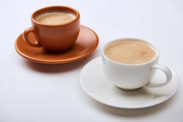 Foyer sélectif de délicieux café avec mousse dans des tasses sur des soucoupes sur fond blanc — Photo de stock