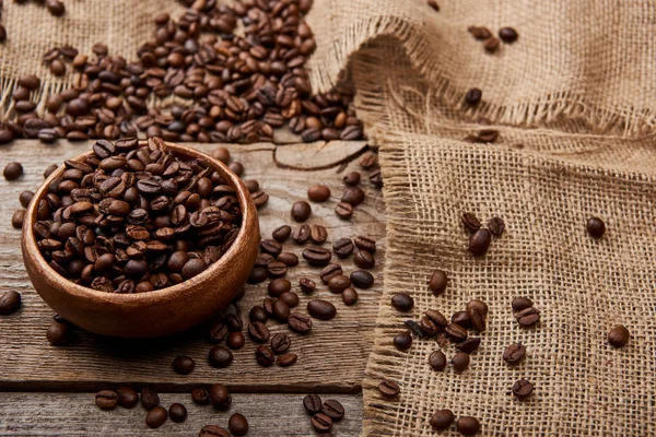 Granos de café tostados frescos en tazón sobre tabla meteorológica de madera con tela de saco - foto de stock