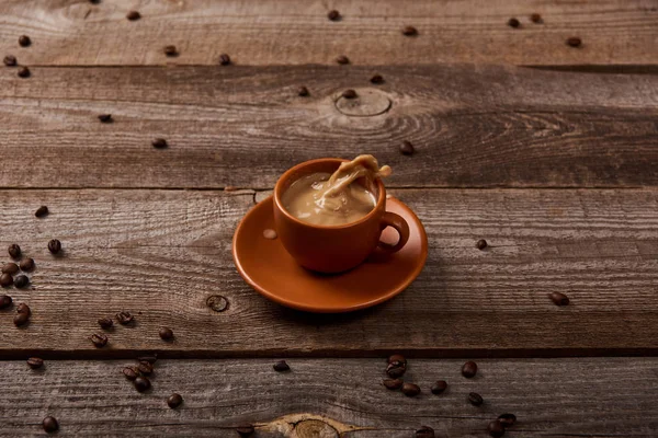 Spruzzi di caffè in tazza sul tavolo di legno con chicchi di caffè sparsi — Foto stock