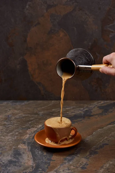 Partial view of man pouring coffee from cezve in cup on marble surface — Stock Photo