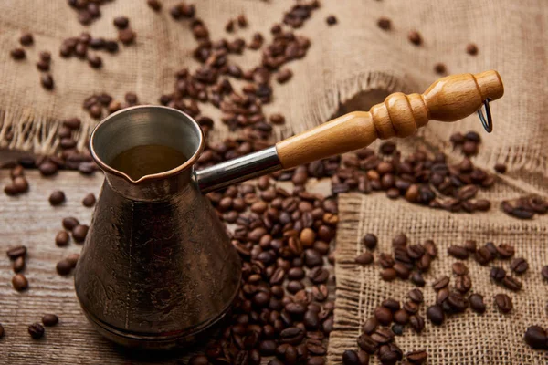 Cezve vicino a chicchi di caffè e sacco su tavolo di legno — Foto stock