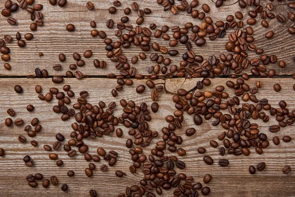 Tavolo in legno intemperie con chicchi di caffè tostato sparsi — Foto stock