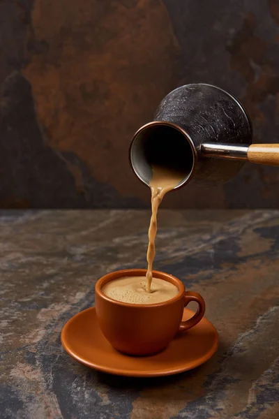 Pouring coffee from cezve into brown cup on marble surface — Stock Photo