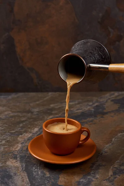 Kaffee aus Cezve in Tasse auf Untertasse auf Marmoroberfläche gießen — Stockfoto