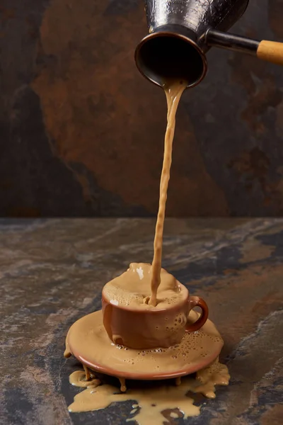 Gießen heißen Kaffee aus Cezve in Tasse mit Pfütze in der Nähe Untertasse auf Marmoroberfläche — Stockfoto