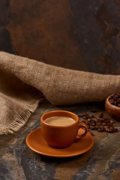 Heißer Kaffee in Tasse auf Untertasse auf Marmoroberfläche in der Nähe von Sacktuch und Bohnen — Stockfoto