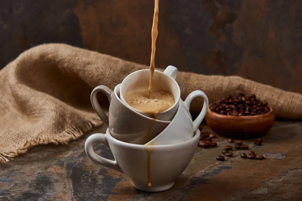 Che fuoriesce caffè caldo da tazze sulla superficie di marmo vicino a sacco e fagioli — Foto stock