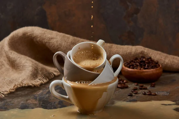 Fließt heißer Kaffee aus Tassen mit Pfütze auf Marmoroberfläche in der Nähe von Sacktuch und Bohnen — Stockfoto