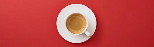 Vista dall'alto di tazza bianca con caffè sul piattino su sfondo rosso, colpo panoramico — Foto stock