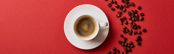 Vue du dessus de délicieux café dans une tasse près de grains torréfiés sur fond rouge, panoramique — Photo de stock