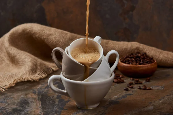 Fließt heißer Kaffee aus Tassen auf Marmoroberfläche in der Nähe von Sacktuch und Bohnen — Stockfoto