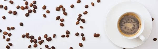 Vista superior del delicioso café en taza cerca de granos tostados dispersos sobre fondo blanco, plano panorámico - foto de stock
