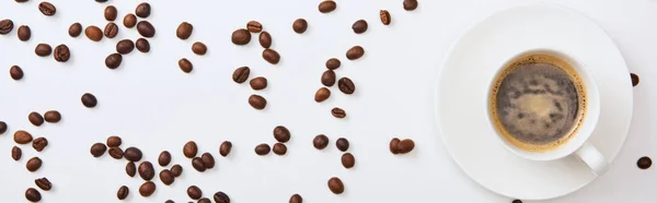 Vista dall'alto di delizioso caffè in tazza vicino a fagioli tostati sparsi su sfondo bianco, colpo panoramico — Foto stock