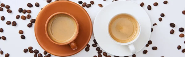 Top view of coffee in white and brown cups on saucers near scattered roasted beans, panoramic shot — Stock Photo