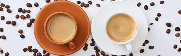 Vista dall'alto del caffè in tazze bianche e marroni su piattini vicino a fagioli tostati sparsi, colpo panoramico — Foto stock