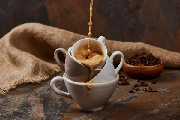 Fließt heißer Kaffee aus Tassen in der Nähe von Sacktuch und Bohnen — Stockfoto