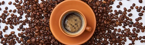 Tiro panorâmico de café delicioso em xícara marrom perto de grãos torrados espalhados no fundo branco — Fotografia de Stock