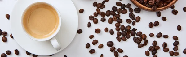 Vue du dessus du café dans la tasse sur la soucoupe près de grains torréfiés dispersés, vue panoramique — Photo de stock