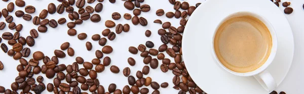 Vue du dessus du café dans la tasse sur la soucoupe près de grains torréfiés dispersés, vue panoramique — Photo de stock