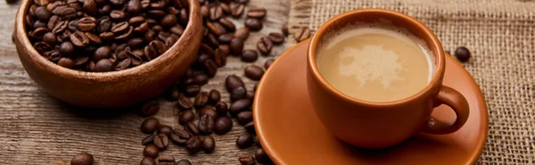 Colpo panoramico di chicchi di caffè in ciotola vicino a tazza di caffè su sfondo di legno — Foto stock