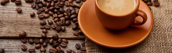 Tiro panorâmico de grãos de café perto de xícara de café em fundo de madeira — Fotografia de Stock