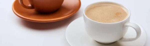 Fuoco selettivo di caffè con schiuma in tazze su piattini su sfondo bianco, colpo panoramico — Foto stock