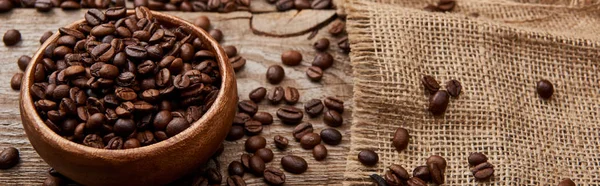 Plano panorámico de granos de café tostados frescos en tazón sobre tabla meteorológica de madera con tela de saco - foto de stock