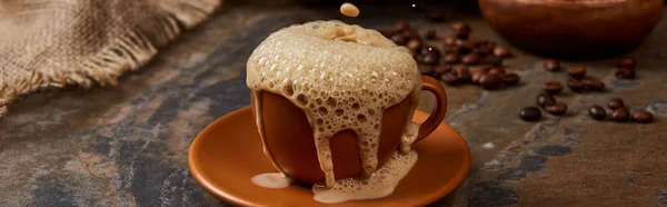 Panoramic shot of coffee foam pouring out of cup on saucer on marble surface — Stock Photo