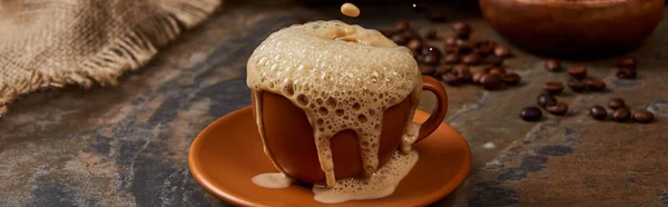 Tiro panorâmico de espuma de café derramando fora do copo no pires na superfície de mármore — Fotografia de Stock
