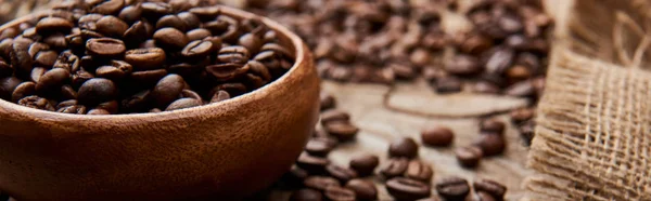 Panoramic shot of roasted coffee beans in bowl on wooden board with sackcloth — Stock Photo