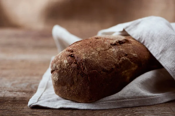 Fresh baked brown bread in white napkin on wooden table — Stock Photo