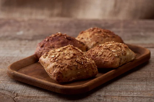 Fresh baked buns with grains on wooden board on table — Stock Photo
