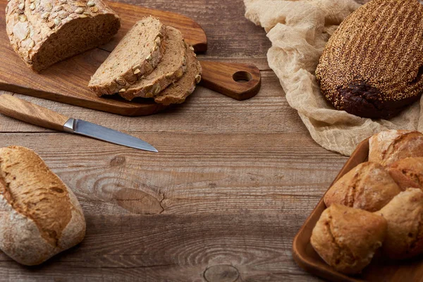 Corte recién horneado y pan entero y bollos en mesa de madera - foto de stock
