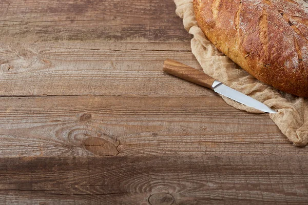 Pane appena sfornato su stoffa vicino a coltello su tavolo di legno — Foto stock