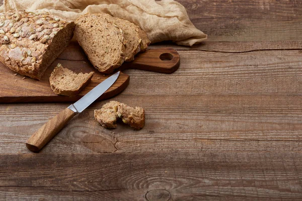 Pão fresco cortado em tábua de corte perto de pano e faca na mesa de madeira — Fotografia de Stock