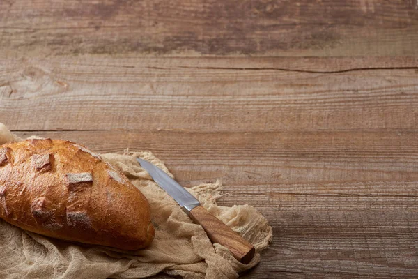 Pane intero fresco su stoffa vicino a coltello su tavolo di legno — Foto stock