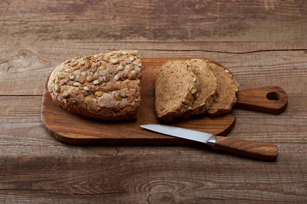 Pão fresco cortado com sementes na tábua de cortar perto da faca na mesa de madeira — Fotografia de Stock