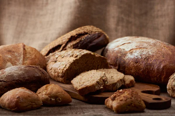 Смачні хліби хліба на дерев'яній дошці з мішковиною на фоні — стокове фото