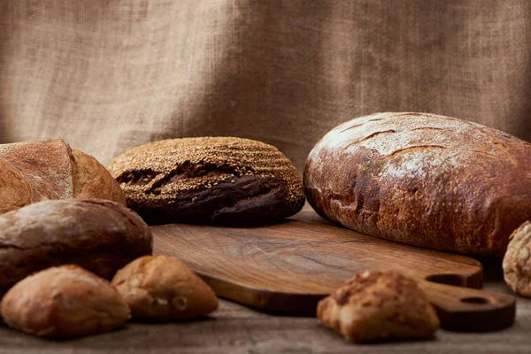 Foyer sélectif de délicieux pains près de planche à découper en bois avec sac sur fond — Photo de stock