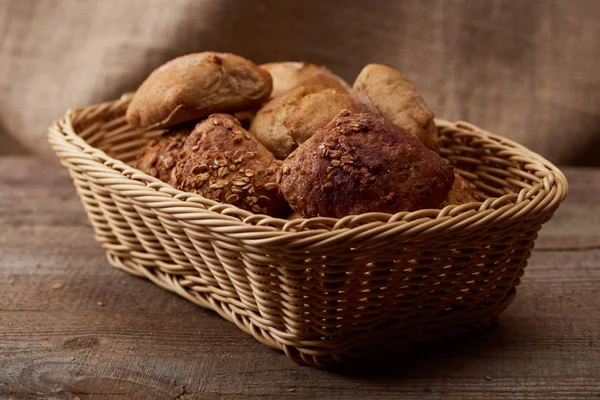 Вкусный хлеб и булочки в плетеной коробке на деревянном столе — стоковое фото