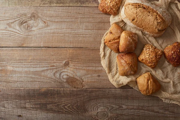 Vista dall'alto di pane appena sfornato e focacce su stoffa su tavola di legno — Foto stock