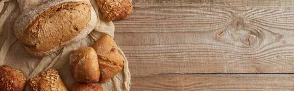 Top view of fresh baked bread and buns on cloth on wooden table, panoramic shot — Stock Photo